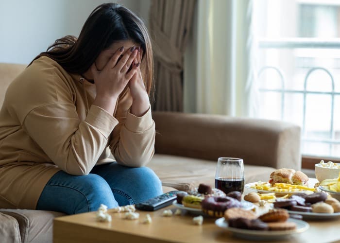 Mulher estressada sentada em sofá olhando para mesa repleta de comida