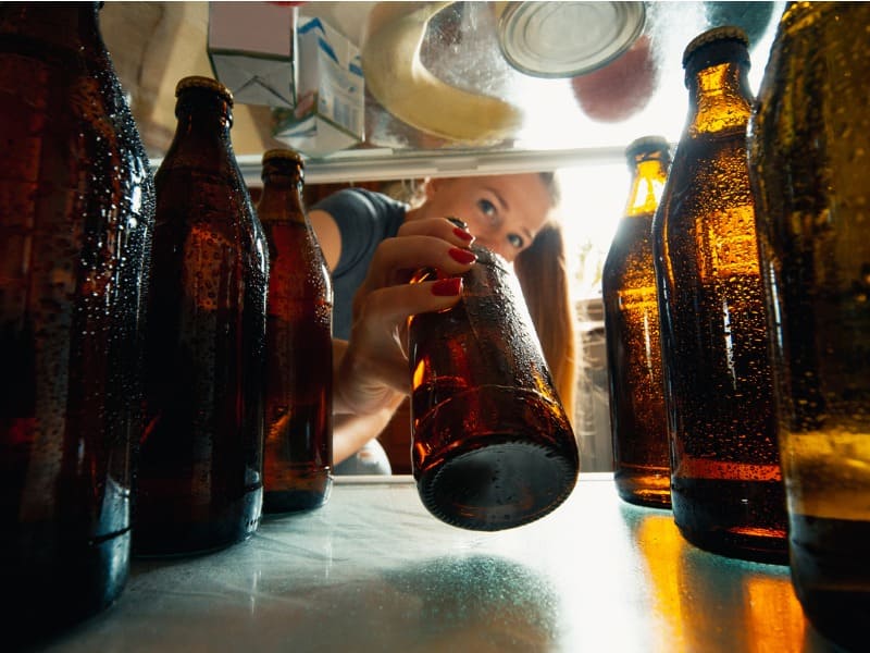 Mulher pegando garrafa de bebida alcoólica da geladeira